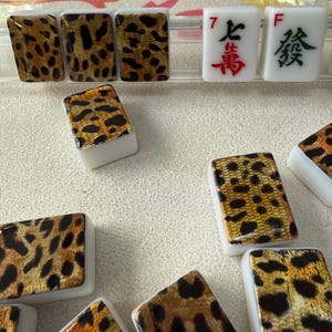 May include: A collection of rectangular Mahjong tiles featuring a white base and a gold and black leopard print pattern on the face. Two tiles display red and green Chinese characters with the letters F and the number 7 printed in the corners.