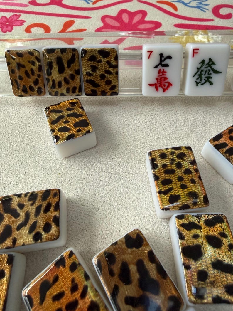 May include: A collection of rectangular Mahjong tiles featuring a white base and a gold and black leopard print pattern on the face. Two tiles display red and green Chinese characters with the letters F and the number 7 printed in the corners.