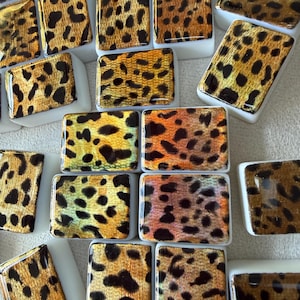 May include: A collection of rectangular tiles featuring a glossy leopard print pattern in shades of gold, bronze, and black. Each tile has a smooth, reflective surface with a white base, arranged in a scattered pattern across the frame.