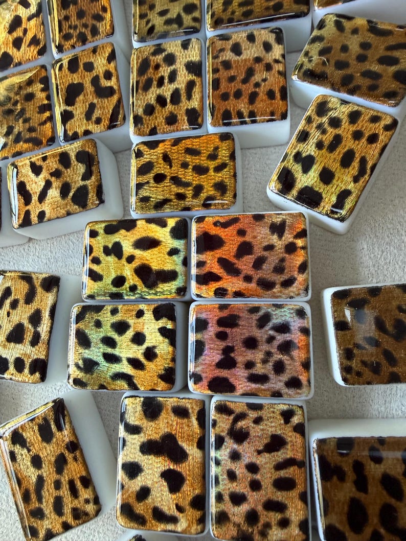May include: A collection of rectangular tiles featuring a glossy leopard print pattern in shades of gold, bronze, and black. Each tile has a smooth, reflective surface with a white base, arranged in a scattered pattern across the frame.