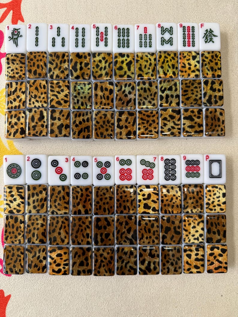 May include: A set of rectangular mahjong tiles featuring a leopard print pattern on the backs. The fronts display various traditional symbols, including bamboo, circles, characters, and the green dragon, with small red numbers 1 through 9 above.