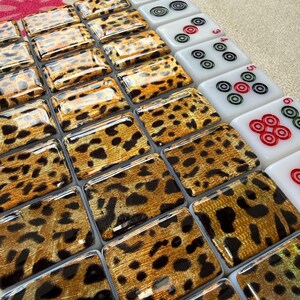 May include: A set of rectangular mahjong tiles arranged in rows. The majority of the tiles feature a glossy gold and black leopard print pattern. A column of white tiles on the right side displays red, green, and black circular dot symbols.
