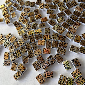 May include: A collection of numerous small, rectangular tiles featuring a brown and black leopard print pattern. Each tile has a glossy finish and a solid white base, arranged in a scattered formation across the frame.