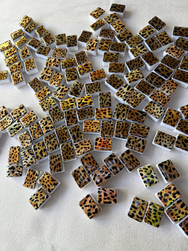 May include: A collection of numerous small, rectangular tiles featuring a brown and black leopard print pattern. Each tile has a glossy finish and a solid white base, arranged in a scattered formation across the frame.