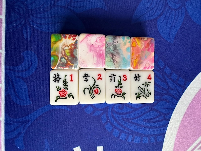 May include: Eight Mahjong tiles. The top row features tiles with colorful abstract designs in shades of yellow, pink, and blue. The bottom row displays white tiles with Chinese characters, numbers, and floral illustrations.
