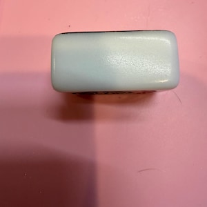 May include: A rectangular mahjong tile with a smooth white surface and rounded edges. The top face is plain white, while the side features a black engraved character design. The tile has a glossy finish and a solid, compact construction.