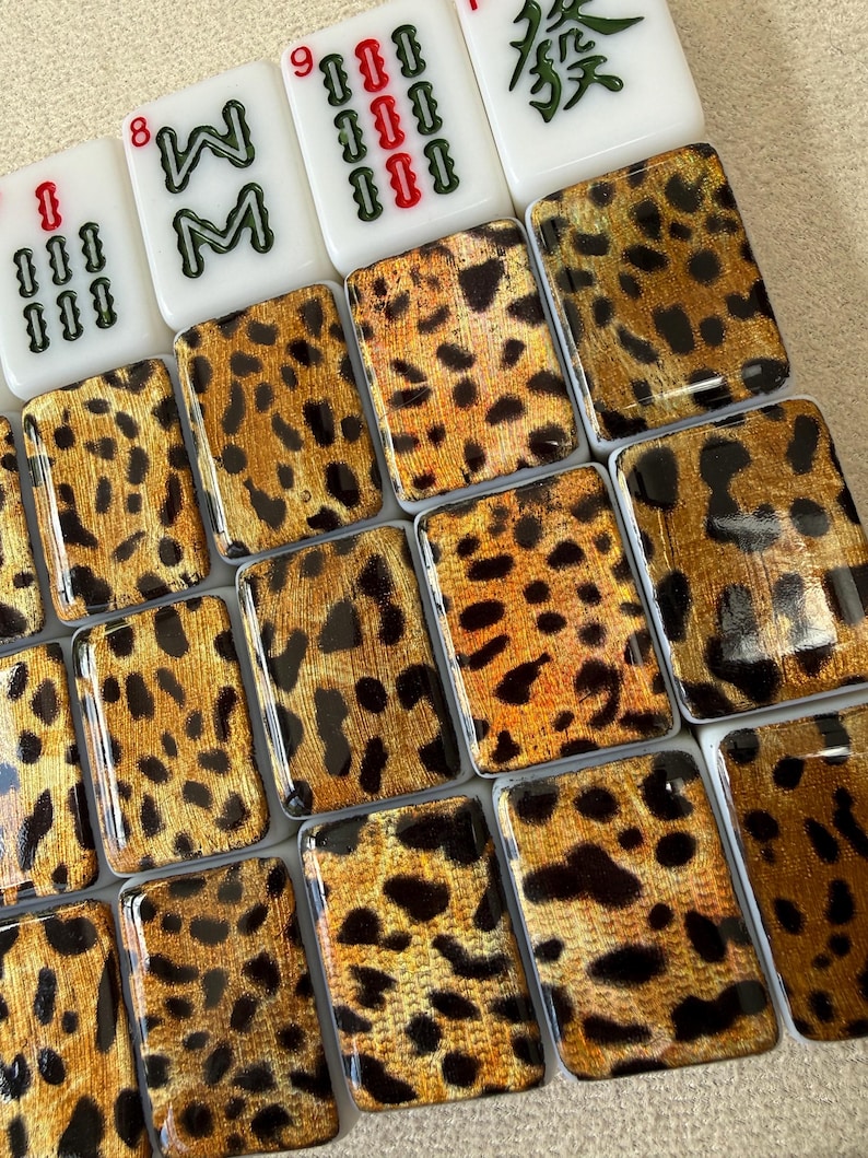 May include: A collection of rectangular mahjong tiles featuring a glossy leopard print pattern in shades of gold, brown, and black. At the top, four white tiles display green and red numerical and character markings, including the number 8 and 9.