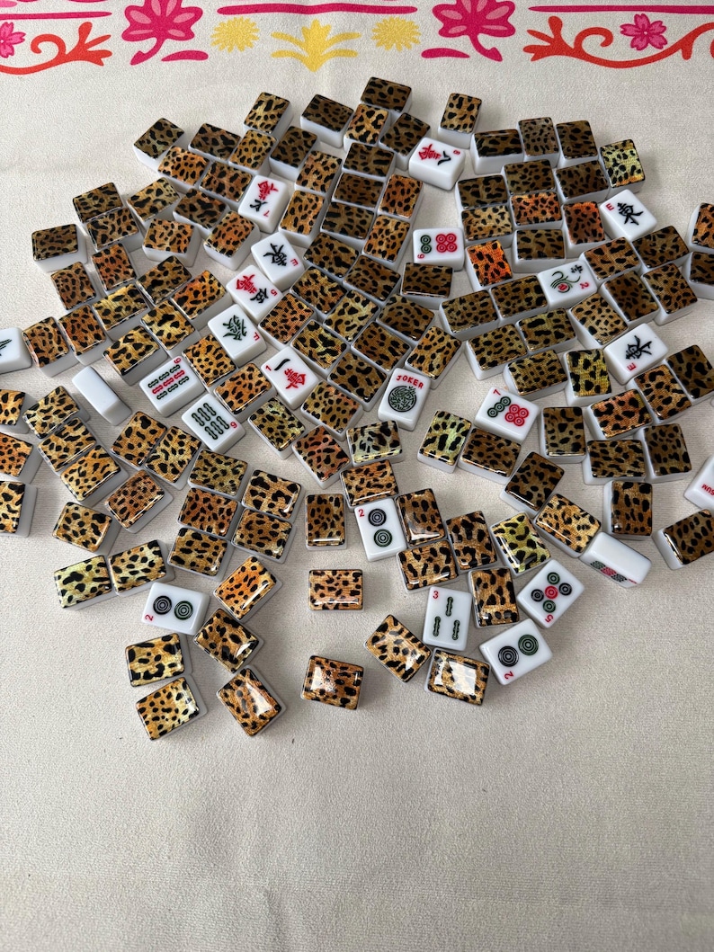 May include: A collection of rectangular Mahjong tiles scattered across a surface. The tiles feature a white base with a black and brown leopard print pattern on the back, while the front faces display various traditional symbols, numbers, and characters.