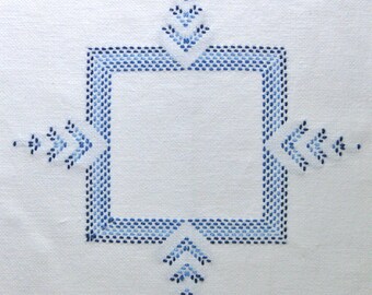 May include: White fabric with a square blue embroidered design. The design features a square border with small, evenly spaced stitches and decorative arrow-like elements at each corner and center of each side.