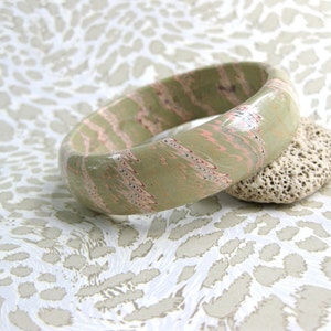 May include: A green and pink marbled bangle bracelet with a white swirl pattern.