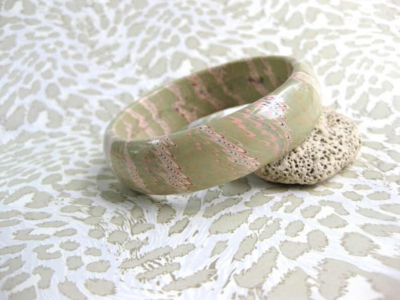 May include: A green and pink marbled bangle bracelet with a white swirl pattern.