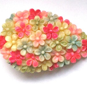 Puede incluir: Un broche vintage con forma de l&aacute;grima, hecho de pl&aacute;stico y con un racimo de flores rosas, verdes y blancas.