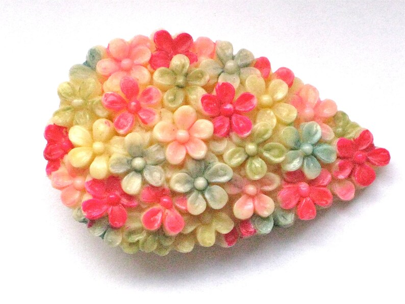 Puede incluir: Un broche vintage con forma de l&aacute;grima, hecho de pl&aacute;stico y con un racimo de flores rosas, verdes y blancas.