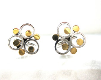 May include: A pair of cufflinks with a modern design. Each cufflink features a cluster of silver-toned circles and gold-toned circular accents. The cufflinks are set against a white background.