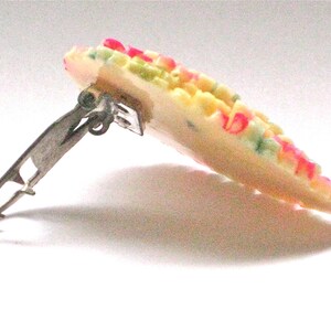 Puede incluir: Una pinza para el pelo de pl&aacute;stico blanco con un dise&ntilde;o floral colorido. La pinza tiene un cierre de metal plateado.