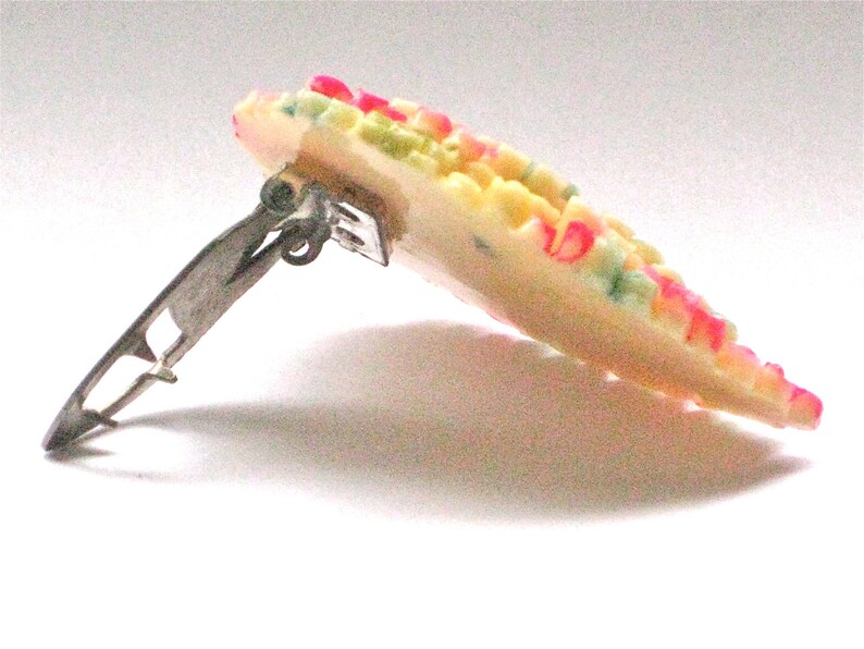 Puede incluir: Una pinza para el pelo de pl&aacute;stico blanco con un dise&ntilde;o floral colorido. La pinza tiene un cierre de metal plateado.