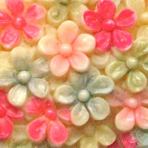 Puede incluir: Primer plano de un grupo de peque&ntilde;as flores de colores pastel. Las flores est&aacute;n hechas de un material liso y brillante y tienen un ligero brillo iridiscente. Las flores est&aacute;n dispuestas en un patr&oacute;n aleatorio, creando un dise&ntilde;o visualmente atractivo y delicado.