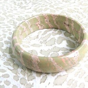 May include: A green and pink bangle bracelet with a swirling pattern. The bracelet is made of wood and has a glossy finish.