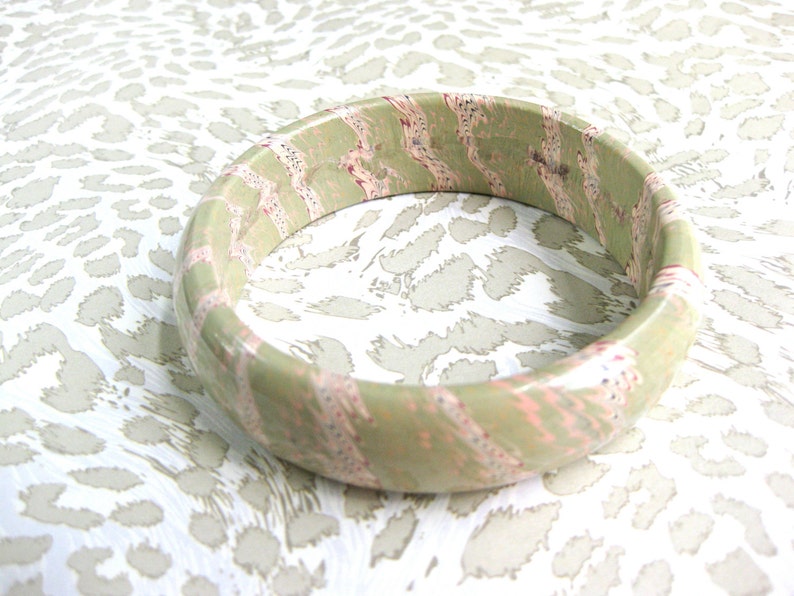 May include: A green and pink bangle bracelet with a swirling pattern. The bracelet is made of wood and has a glossy finish.