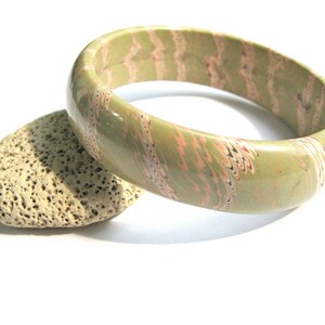 May include: A green and pink marbled bangle bracelet. The bracelet is made of a smooth, glossy material and has a unique marbled pattern.