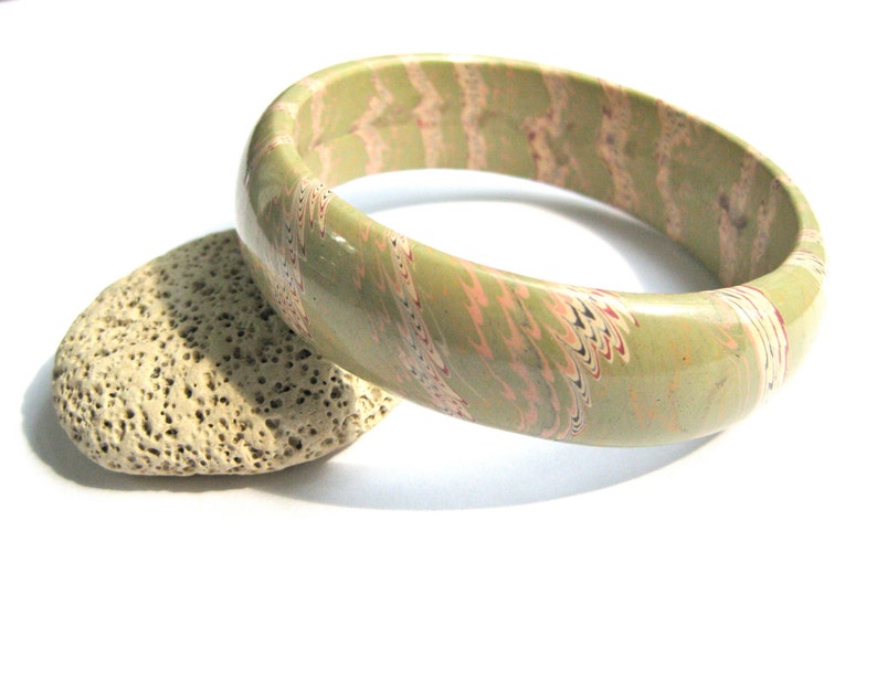 May include: A green and pink marbled bangle bracelet. The bracelet is made of a smooth, glossy material and has a unique marbled pattern.