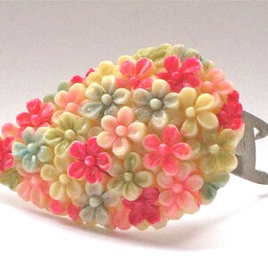 Puede incluir: Un broche vintage con forma de racimo de flores. Las flores est&aacute;n hechas de pl&aacute;stico y son de color rosa, crema y verde.
