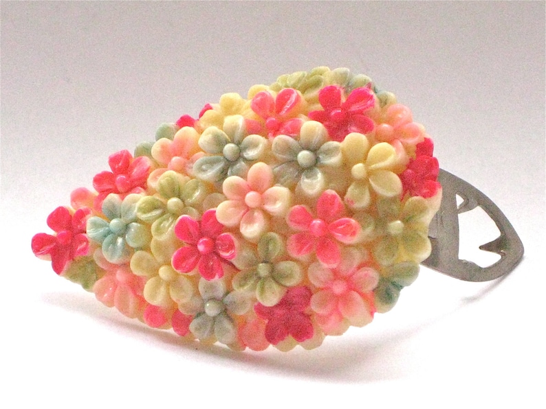 Puede incluir: Un broche vintage con forma de racimo de flores. Las flores est&aacute;n hechas de pl&aacute;stico y son de color rosa, crema y verde.