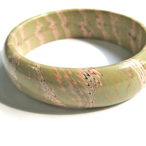 May include: A green, pink, and white marbled bangle bracelet. The bracelet is made of a smooth, hard material and has a glossy finish.