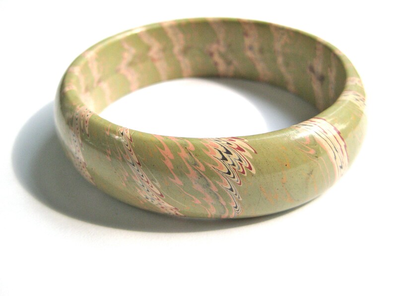 May include: A green, pink, and white marbled bangle bracelet. The bracelet is made of a smooth, hard material and has a glossy finish.