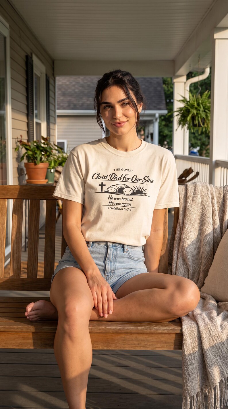 May include: A cream-coloured short-sleeve t-shirt featuring black text that reads THE GOSPEL Christ Died For Our Sins, He was buried, He rose again, 1 Corinthians 15:3-4, accompanied by a graphic of a cross, an open tomb, and a rising sun.