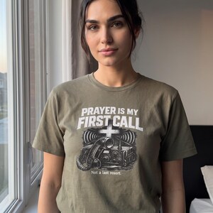 Puede incluir: Una camiseta de manga corta color verde oliva con un gr&aacute;fico de un auricular de radio antiguo y el texto PRAYER IS MY FIRST CALL y Not a last resort. El dise&ntilde;o incluye un s&iacute;mbolo de cruz sobre la radio y l&iacute;neas de ondas de se&ntilde;al.
