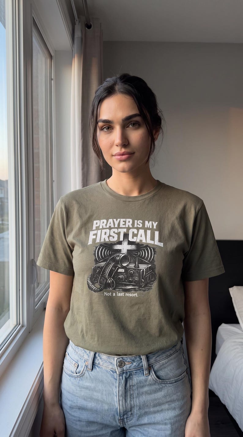 Puede incluir: Una camiseta de manga corta color verde oliva con un gr&aacute;fico de un auricular de radio antiguo y el texto PRAYER IS MY FIRST CALL y Not a last resort. El dise&ntilde;o incluye un s&iacute;mbolo de cruz sobre la radio y l&iacute;neas de ondas de se&ntilde;al.