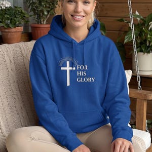 May include: A royal blue hooded sweatshirt featuring a white graphic of a cross with a sunburst design above it and the text "FOR HIS GLORY" printed in white lettering on the front center, including a front kangaroo pocket and long sleeves.