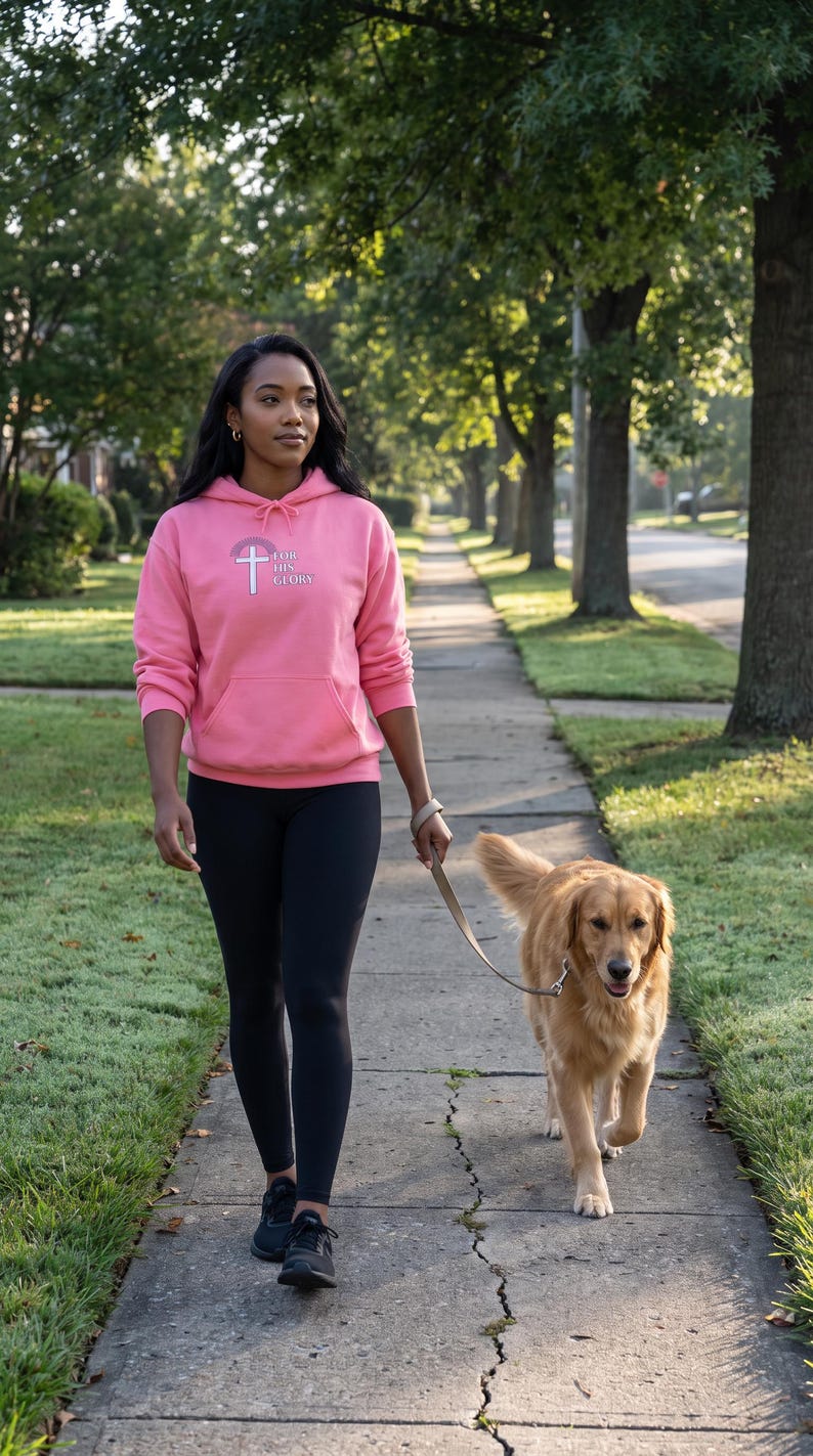 May include: A bright pink hooded sweatshirt featuring a white cross graphic and the text "FOR HIS GLORY" on the chest, paired with black leggings and black athletic sneakers, while holding a tan leather leash attached to a golden retriever.