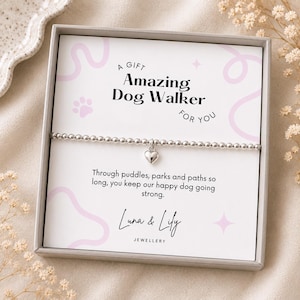 May include: A silver-toned beaded bracelet with a small heart charm, presented on a white card inside a grey box. The card features the text A GIFT Amazing Dog Walker FOR YOU, a paw print, and the poem Through puddles, parks and paths so long, you keep our happy dog going strong. Luna & Lily JEWELLERY is printed at the bottom.