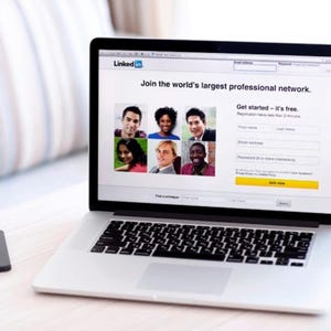 May include: A silver laptop displaying the LinkedIn homepage with a grid of six diverse professional portraits, a registration form, and the text Join the world's largest professional network. A small black smartphone sits to the left of the laptop.