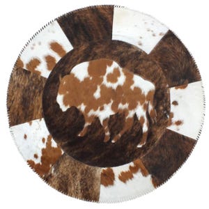May include: A circular rug constructed from stitched panels of cowhide in shades of brown, white, and tan. The central portion features a silhouette of a bison, while the outer border consists of alternating rectangular patches of hide.