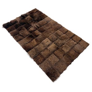 May include: A rectangular rug constructed from numerous square patches of dark brown, long-pile fur. The individual squares are stitched together in a grid pattern, creating a textured, multi-tonal surface with varying shades of brown throughout.