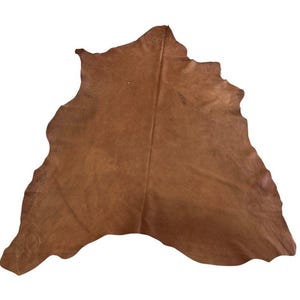May include: A large, irregularly shaped piece of natural brown leather hide with a smooth, matte surface. The hide features a distinct central crease running vertically, with natural, uneven edges and subtle variations in the tan color.