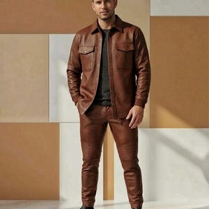 Puede incluir: Una camisa chaqueta de cuero marr&oacute;n con dos bolsillos en el pecho y pantalones de cuero marr&oacute;n a juego. Los pantalones tienen detalles acanalados en las rodillas. El conjunto se completa con zapatillas negras. El fondo es una mezcla de paneles marrones, beige y blancos.