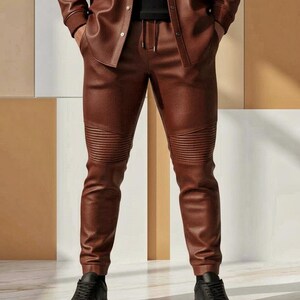 Puede incluir: Conjunto de chaqueta y pantal&oacute;n de cuero marr&oacute;n. El pantal&oacute;n tiene cintura con cord&oacute;n y detalles acanalados en las rodillas. El conjunto se combina con zapatillas negras. Un look elegante y moderno.