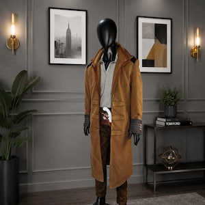 Könnte beinhalten: Ein brauner Wildledermantel mit grauem Hemd und brauner Hose an einer Schaufensterpuppe. Der Mantel hat einen kontrastierenden braunen Kragen und Manschetten. Die Schaufensterpuppe trägt schwarze Handschuhe und Stiefel. Das Outfit wird auf einem grauen Teppich präsentiert.