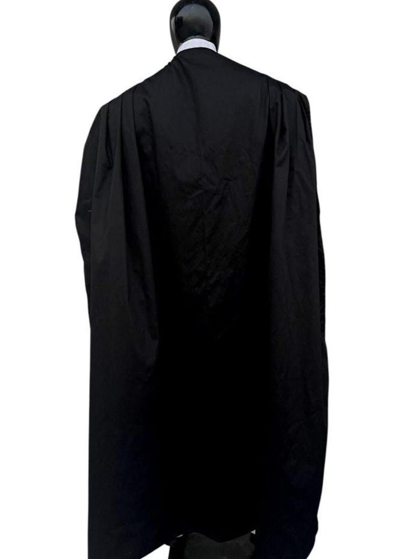 Puede incluir: Una toga acad&eacute;mica larga de color negro con un dise&ntilde;o de hombros estructurado y pliegues verticales profundos que se extienden por la espalda. La prenda se muestra sobre un maniqu&iacute;, exhibiendo un cuello alto y tejido negro opaco.