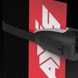 May include: A black and white object with a red and white logo is secured with a black strap. The object has a cylindrical shape with a white accent and a rectangular black panel. The background is black.