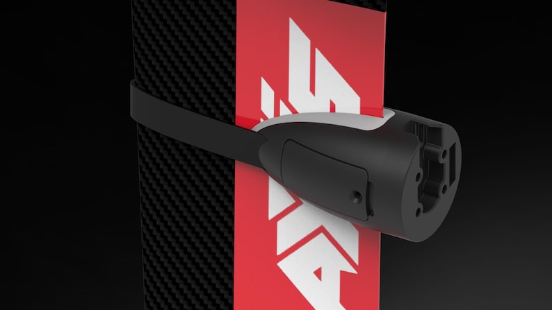 May include: A black and white object with a red and white logo is secured with a black strap. The object has a cylindrical shape with a white accent and a rectangular black panel. The background is black.