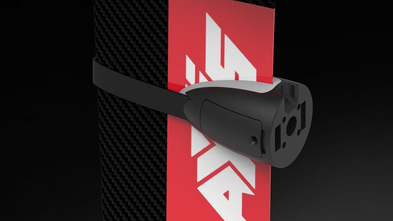 May include: A black and white device with a strap, attached to a red and white surface. The device has a cylindrical shape with a black body and a white top. The surface has a carbon fiber pattern.