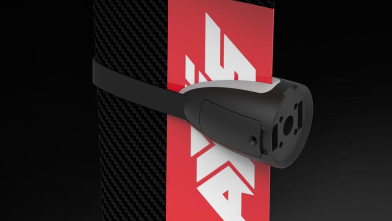 May include: A black and white device with a strap is attached to a red and white surface. The device has a rounded shape with a rectangular section and a circular opening. The background is black.
