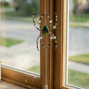 Può includere: Un ornamento decorativo a forma di ragno realizzato con perline verdi, nere, bianche e trasparenti, con un corpo centrale costituito da una perlina verde. Il ragno è sospeso a una catenella in metallo argentato con un pendente in cristallo sfaccettato.