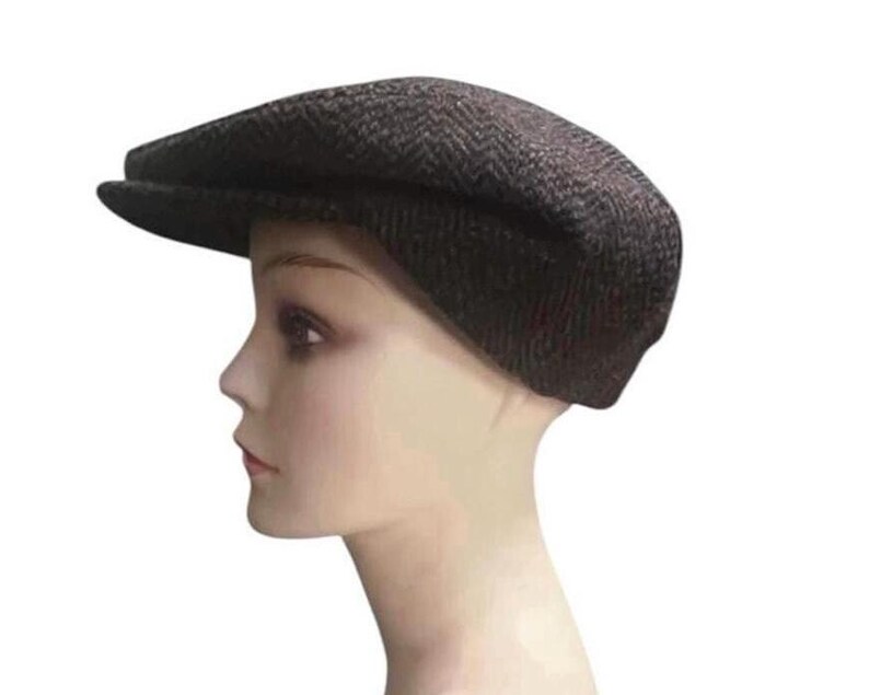 May include: A dark brown flat cap featuring a subtle herringbone pattern. The cap has a rounded crown and a short, stiff brim extending from the front. The fabric displays a textured weave with darker brown and black threads throughout the design.