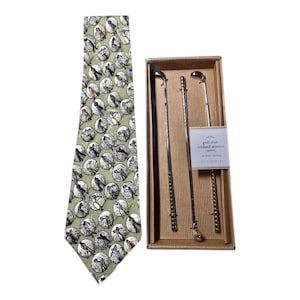 May include: A light green necktie featuring a repeating pattern of golfers inside white circles, paired with a set of three silver-toned metal golf club cocktail stirrers housed in a rectangular cardboard box labeled golf club cocktail stirrers.